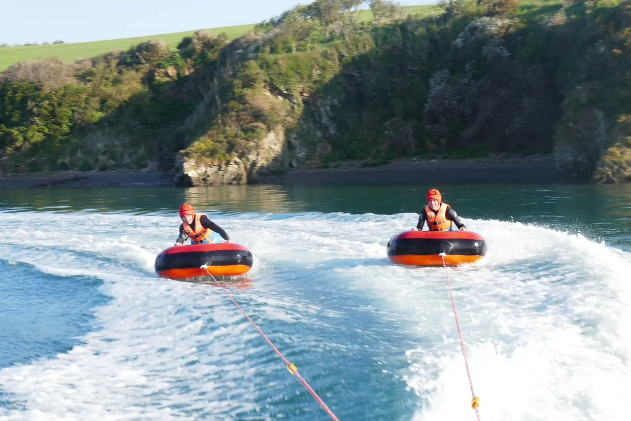 two people riding the chariots on the camel estuary being towed by camel ski school motorboat