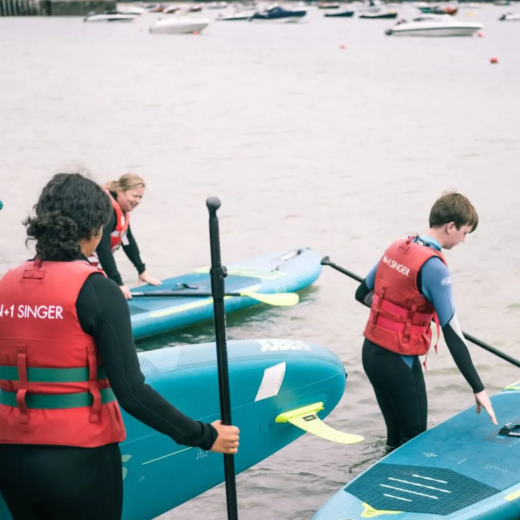 a group going out to paddleboard in rock, camel estuary. carrying their boards into the water