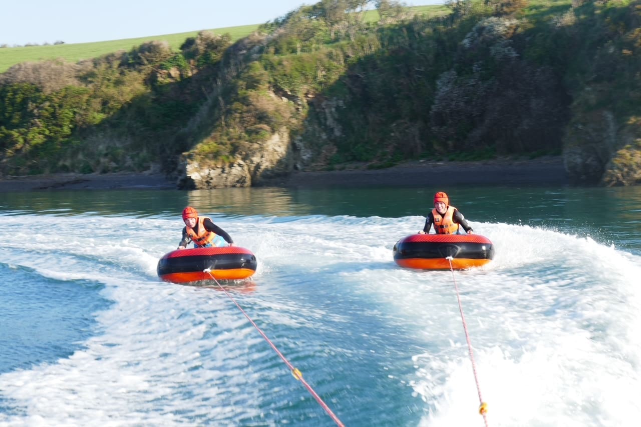 two people riding the chariots on the camel estuary being towed by camel ski school motorboat