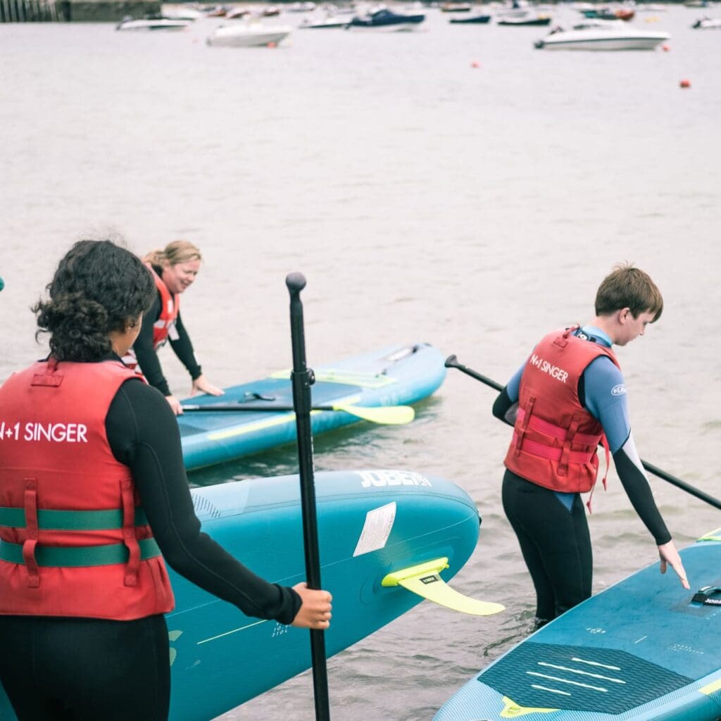 Top places to Paddleboard in Cornwall: The Best Places to Explore - Camel Ski School a group going out to paddleboard in rock, camel estuary. carrying their boards into the water